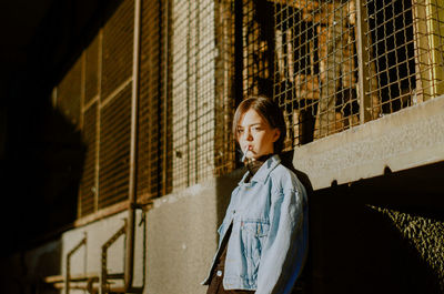 Young woman looking away while standing against building in city