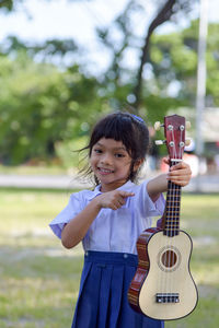 Portrait of smiling girl pointing at ukulele while standing at park