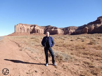 Full length of man standing on rock against clear blue sky