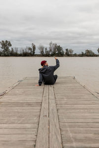 Rear view of man sitting on wood against sky