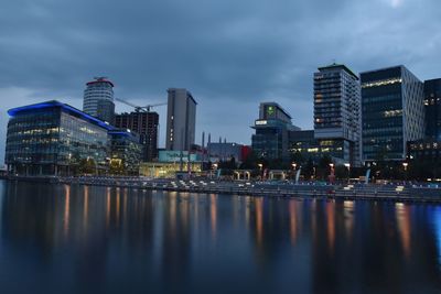 Illuminated buildings by river against sky