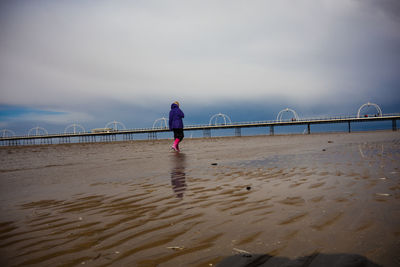 Person from behind walking through wet sand at low tide