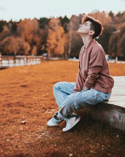 Young woman looking away while sitting on land
