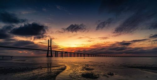 Bridge over sea against dramatic sky during sunset