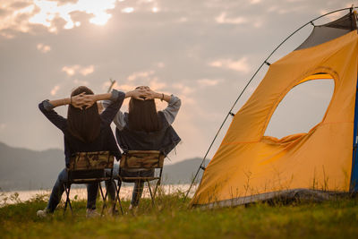 Men in tent on field against sky during sunset