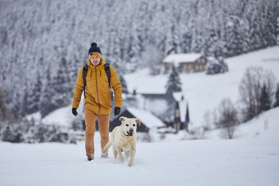 Full length of man walking with dog on snow covered land