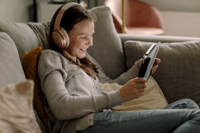 Happy teenage girl on sofa watching movie through digital tablet at home