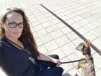 Portrait of woman with dog at pavement on sunny day