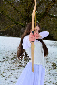 Girl standing in nature with bow and arrow in snow