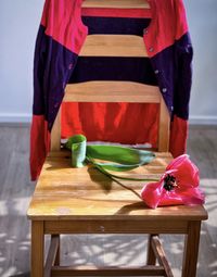 Pink tulip flower on wooden chair with colorful cardigan draped over the back of chair.