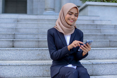 Smiling young man using mobile phone while sitting on staircase