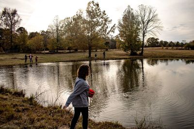 Girl throwing fish food in lake against trees