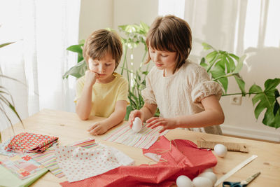 Top view of a boy and a girl, brother and sister crafting easter eggs at home from fabric 