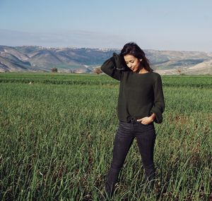 Young woman with hand in hair standing on agricultural field against sky