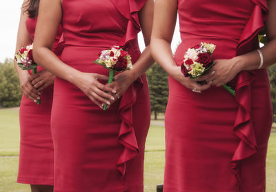 Midsection of bridesmaids holding bouquets in lawn