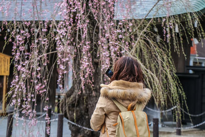 Close-up of young woman photographing with smart phone while standing against tree