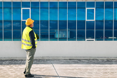 Middle aged bearded supervisor in hardhat and safety vest with tablet on building site. 