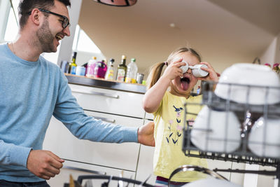 Playful daughter and father clearing dishwasher