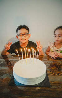 A young boy is celebrating birthday together with little sister. colourful candles on white cake.