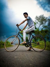 Portrait of young man riding bicycle against sky