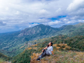 Woman with eyes closed smiling while sitting on mountain