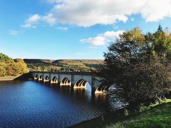 Arch bridge over river against cloudy sky