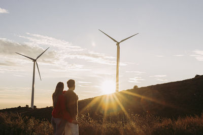 Couple holding hands looking at wind park at sunset