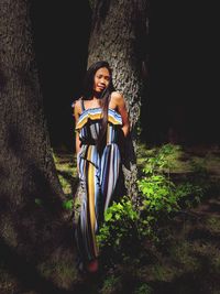 Portrait of woman standing against tree trunk in forest