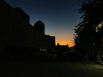 Cars on road amidst buildings against sky at sunset