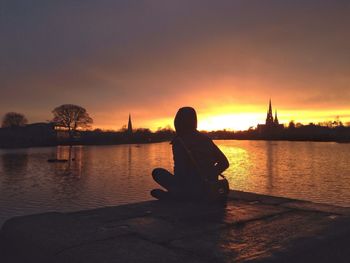 Silhouette of man sitting on river at sunset