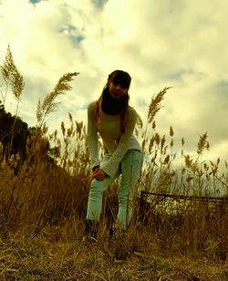 Young woman sitting on field against sky