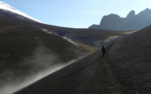 Rear view of man walking on mountain against sky