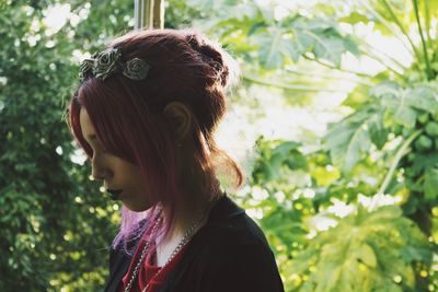 Side view of woman wearing artificial flowers while standing against plants