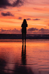 Rear view of silhouette standing on beach during sunset