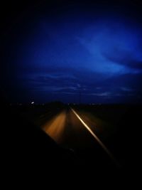 Road amidst silhouette landscape against sky at night