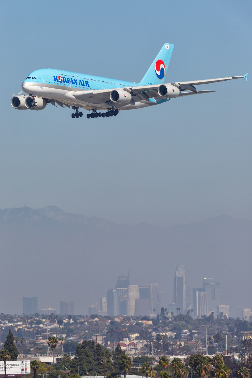 AIRPLANE FLYING OVER CITYSCAPE AGAINST CLEAR SKY