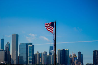 Flag against modern buildings in city against blue sky
