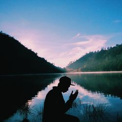 Silhouette man by lake against sky