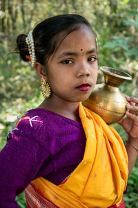 A tribal teenage girl is walking in the woods to fetch water in a brass pitcher