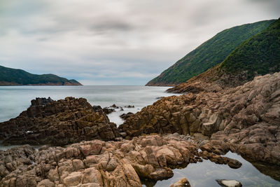 Scenic view of rocks by sea against sky