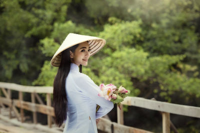 Woman in hat standing on footbridge against trees