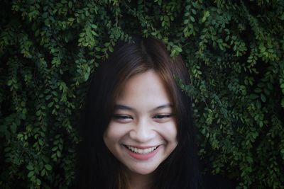 Close-up smiling young woman against leaves