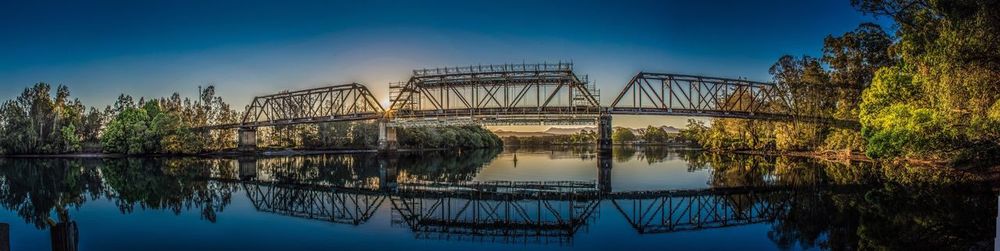 Reflection of trees on bridge against sky