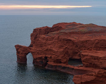 Rock formation in sea against sky during sunset