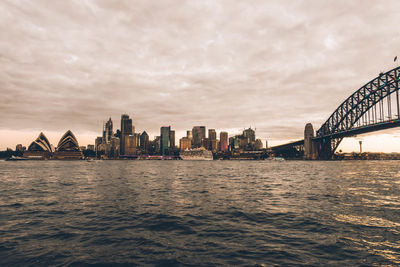 View of city at waterfront against cloudy sky