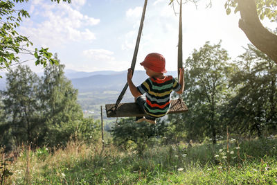 Rear view of boy sitting on land against sky