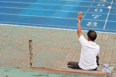 Rear view of man sitting with arm raised by running track