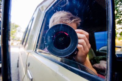 Reflection of man with camera on car side-view mirror