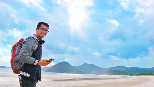 Young man using mobile phone against sky