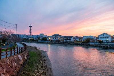 Buildings by river against sky during sunset